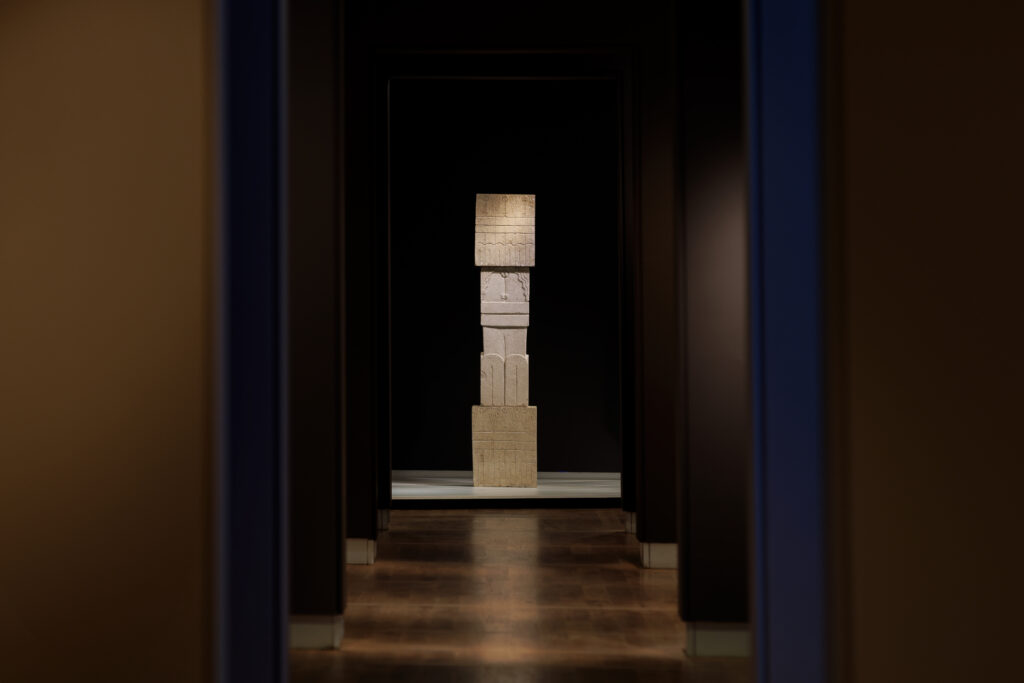 Stone sculpture by the artist Brancusi displayed at the back of a gallery with black walls and subdued lighting.